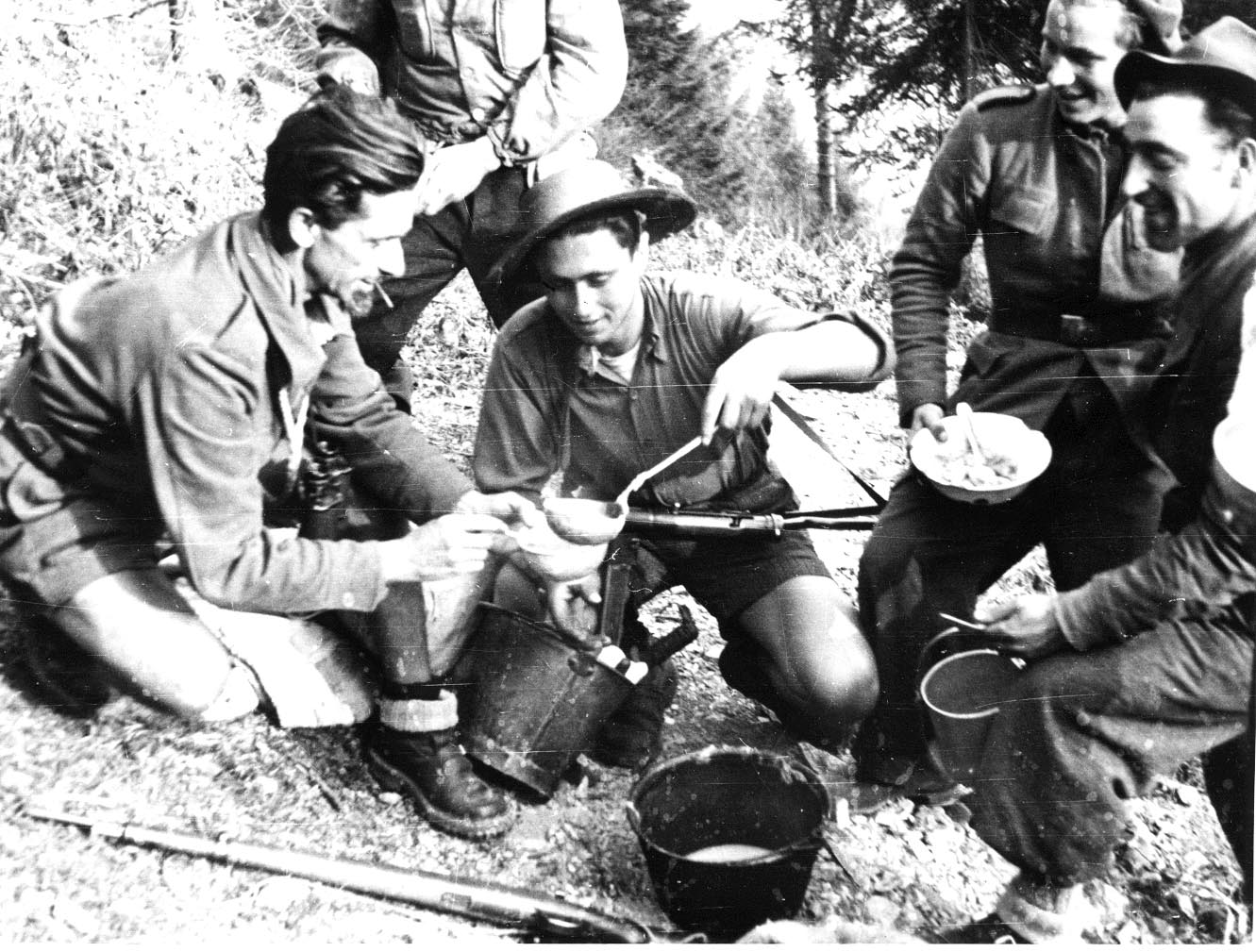 Partigiani. Dalla loro lotta, le basi per la conquista della Costituzione. Nella foto, il partigiano Luigi Tarzia (Tarzan) mentre distribuisce il rancio al comandante Montagna e ai partigiani della 53ª Brigata Garibaldi nel Bergamasco